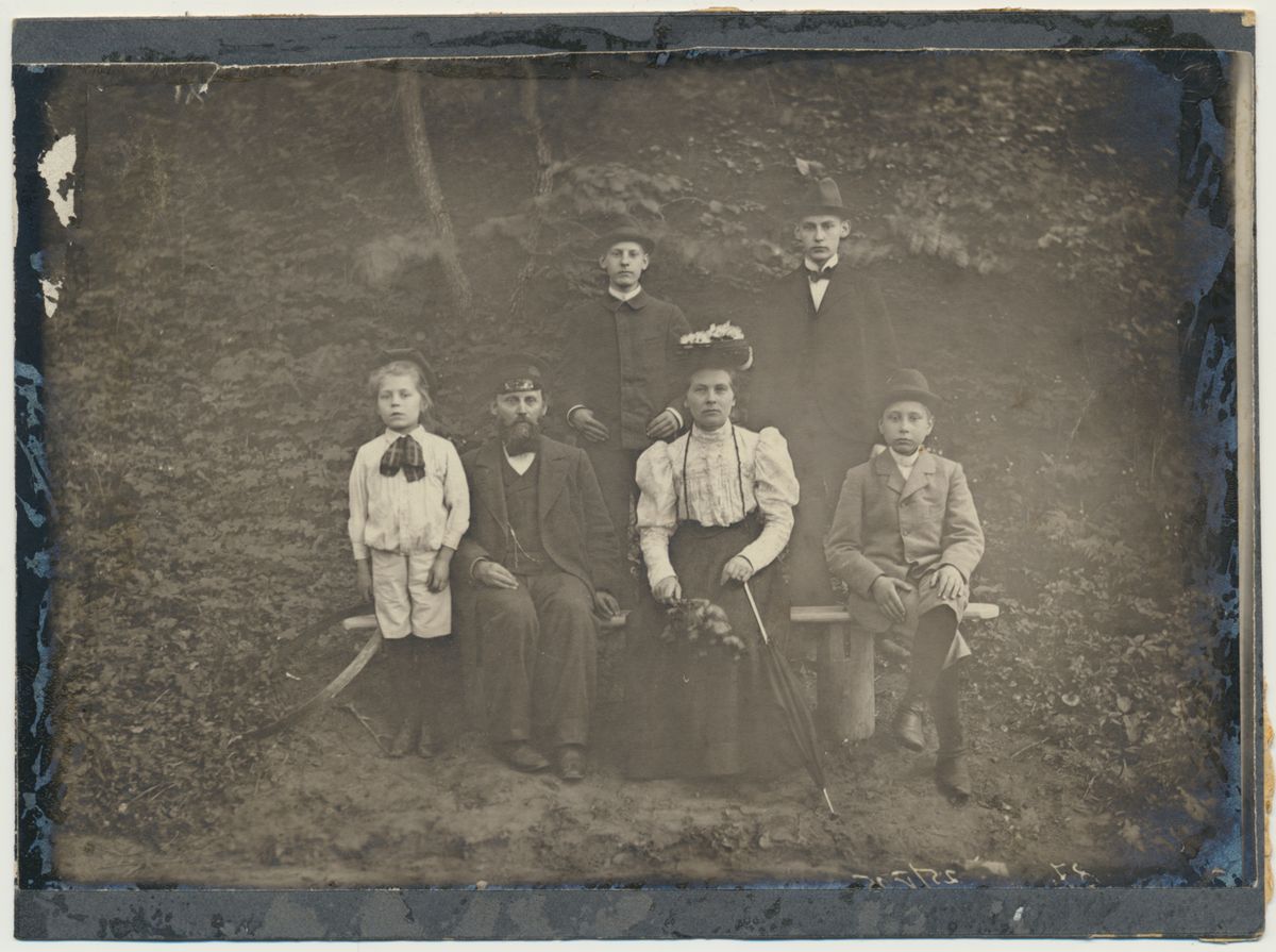 Outdoor group photo, c. 1903: a bearded man and a woman in a flowered hat seated on a bench with two boys, two older boys standing behind.