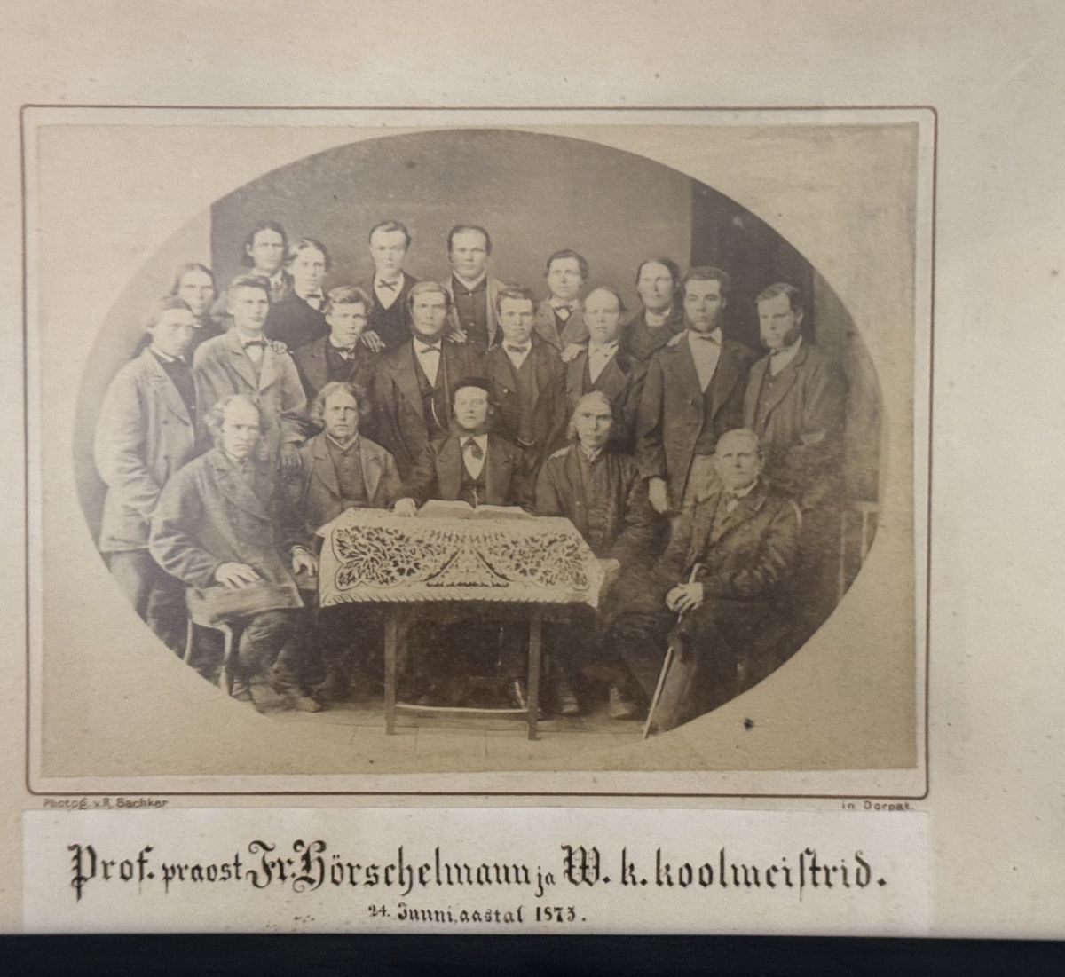 Oval group photo of about thirty men around a table with a lace cloth, captioned in ink beneath.