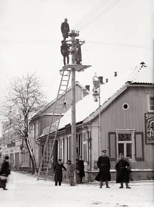 Hans Leoke, in a dark coat and with a beard, in front of his shop at Tartu 11 in 1912, while electric lines are being strung. The EVE building, now the Grand Ho